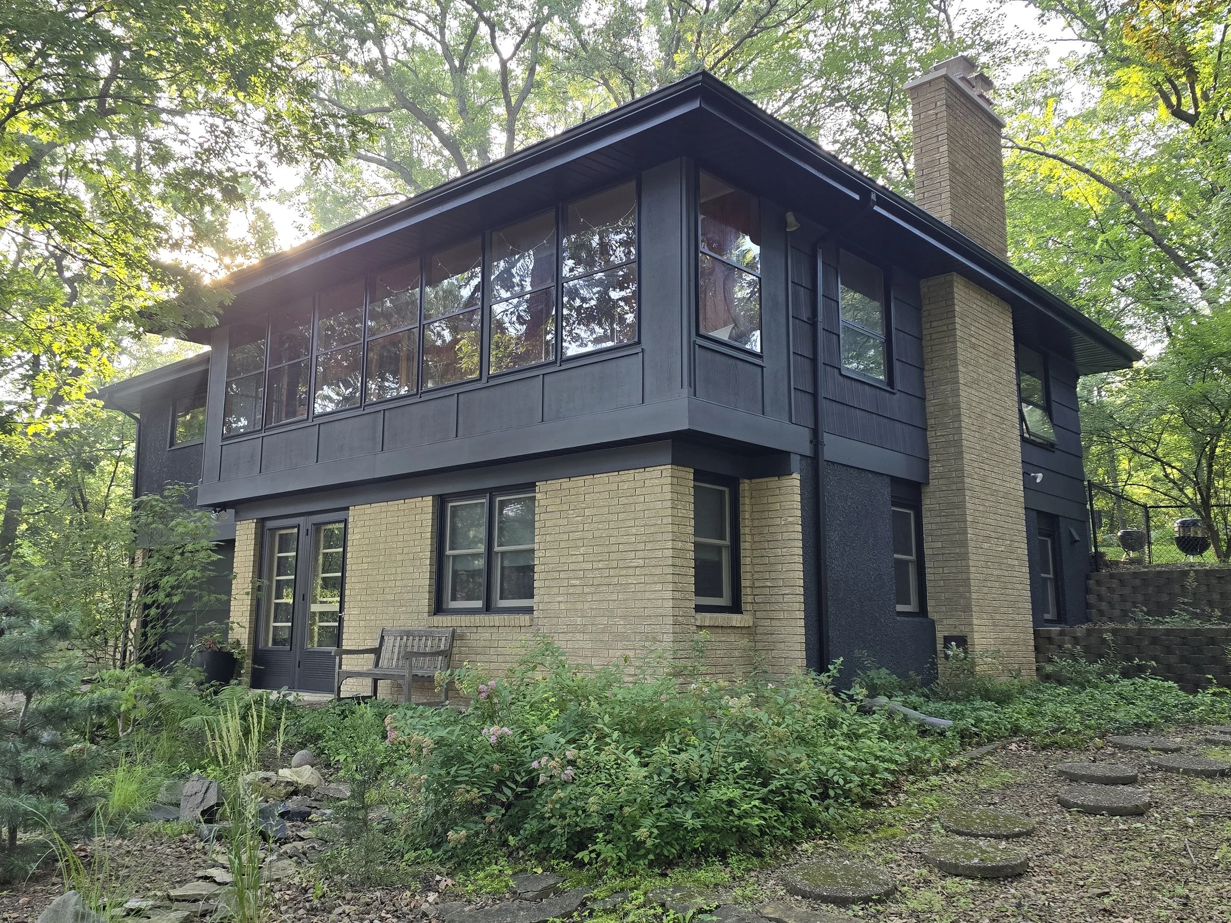 Modern exterior house painting project in Edina, MN featuring dark siding and trim on a wooded mid-century home