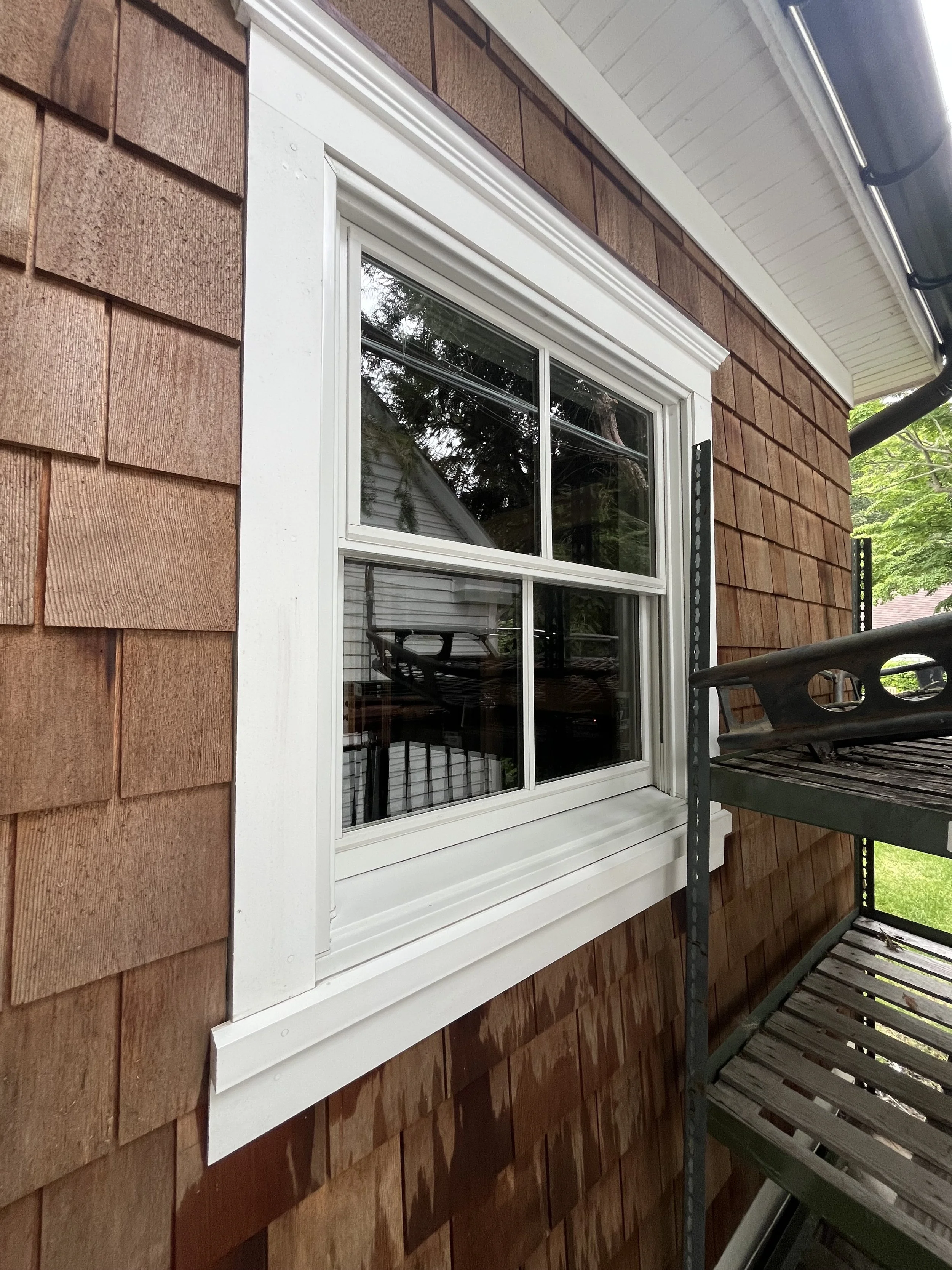 Close-up of a window on a house with wooden shingle siding, under an overhang, with scaffolding nearby.
