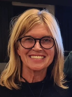 A smiling woman with blonde hair, wearing glasses, in an indoor setting.