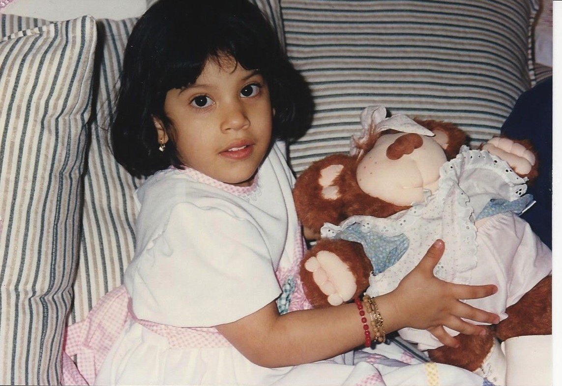 Young girl holding a brown stuffed animal, sitting on a bed with striped pillows.