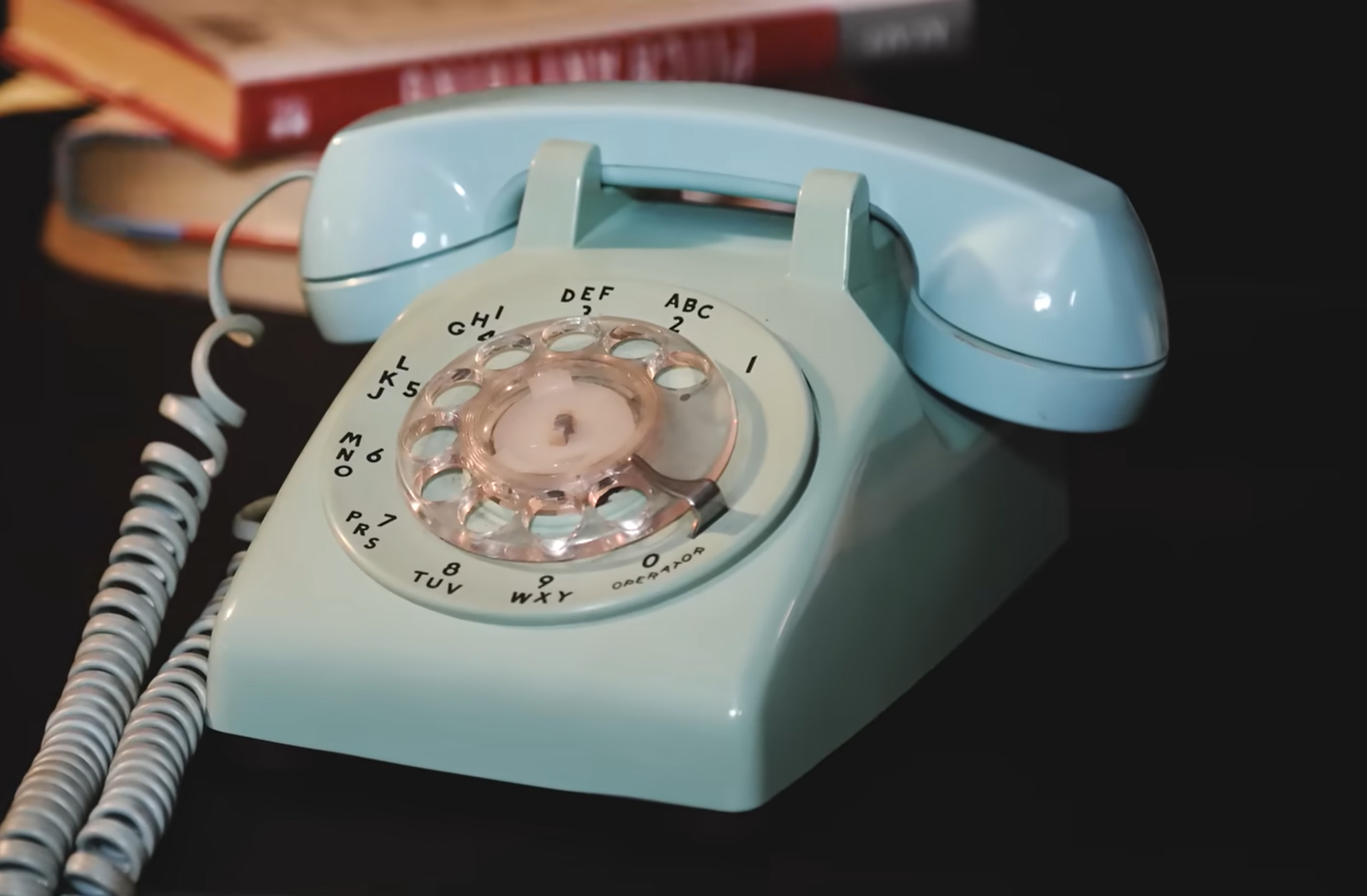 Vintage blue rotary dial telephone on a desk with books in the background.