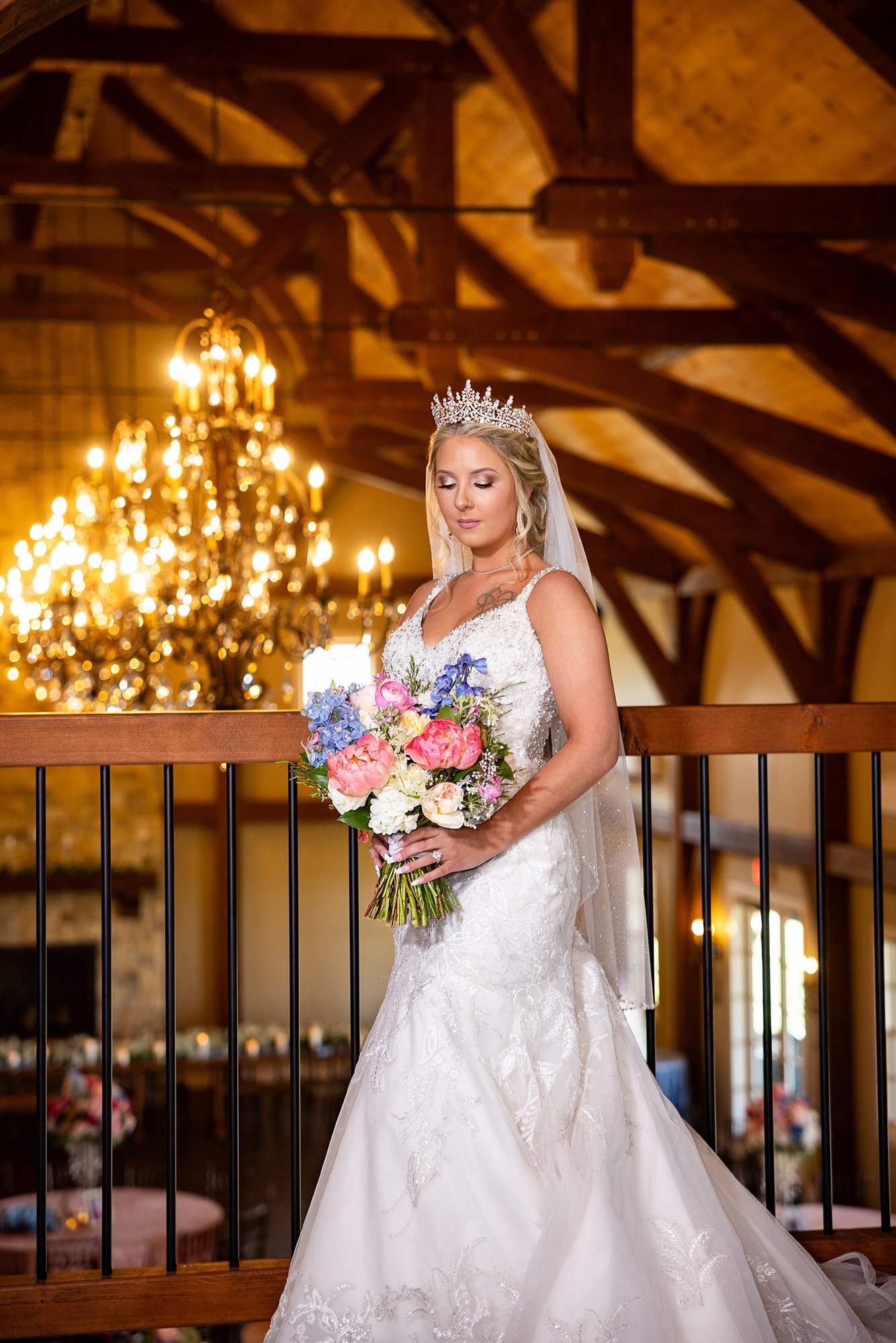A bride in a white wedding dress and tiara holding a bouquet of colorful flowers. Wedding Venue: The English Barn, a one-of-a-kind castle-inspired venue full of rustic elegance and charm located in Louisburg, KS -- just South of KC.