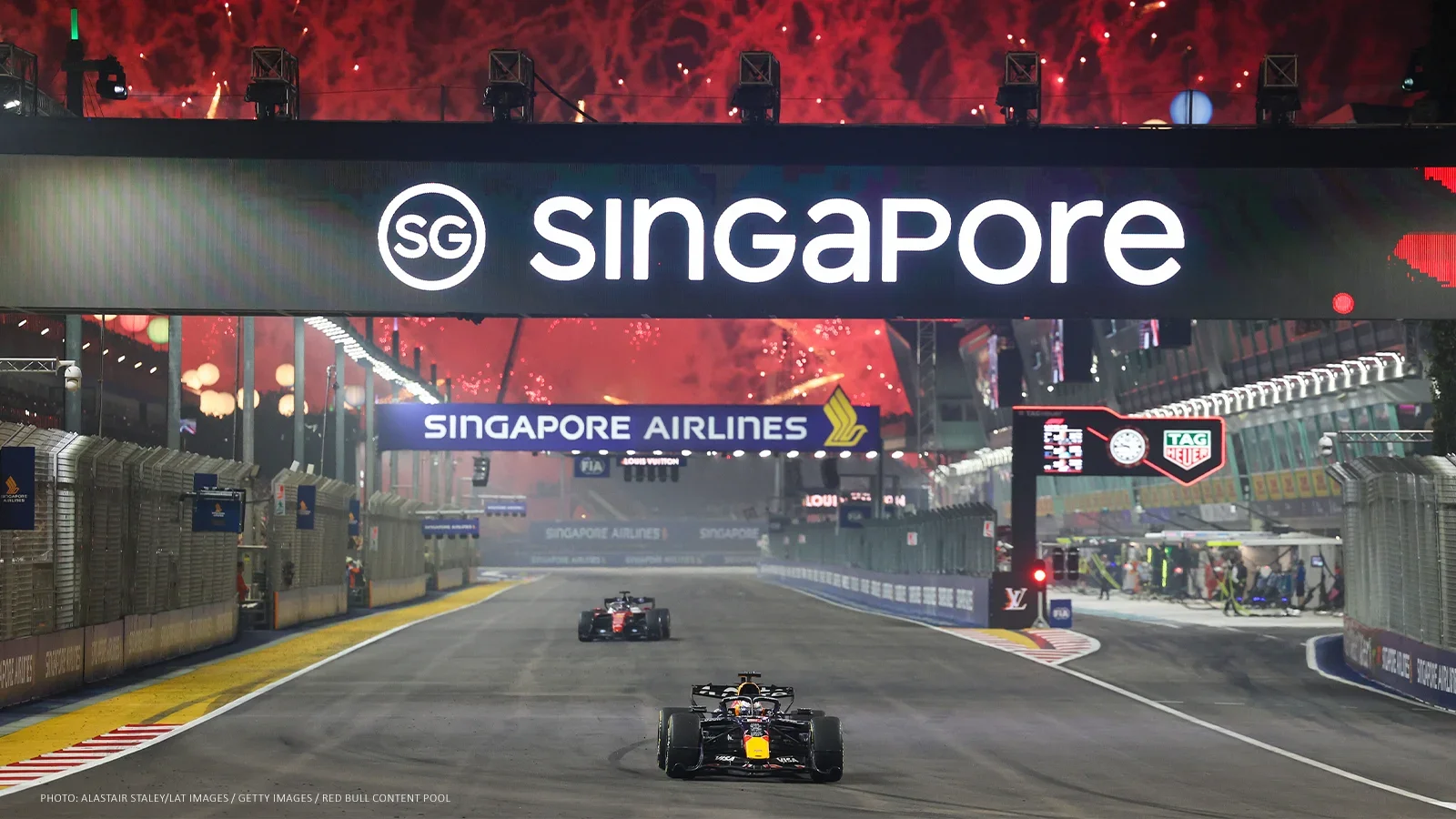 Max Verstappen takes the chequered flag at the 2026 Singapore Grand Prix beneath the Singapore sign as fireworks light the sky.