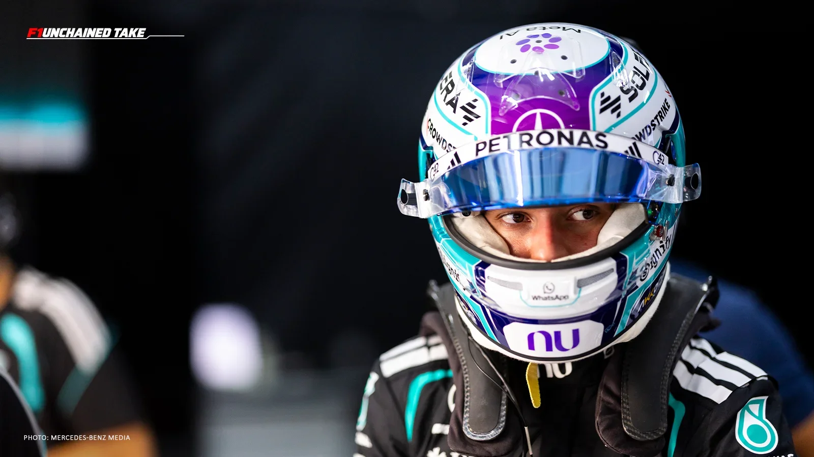 Kimi Antonelli wearing his Mercedes helmet and race suit inside the team garage, with F1Unchained Take branding in the upper-left corner.