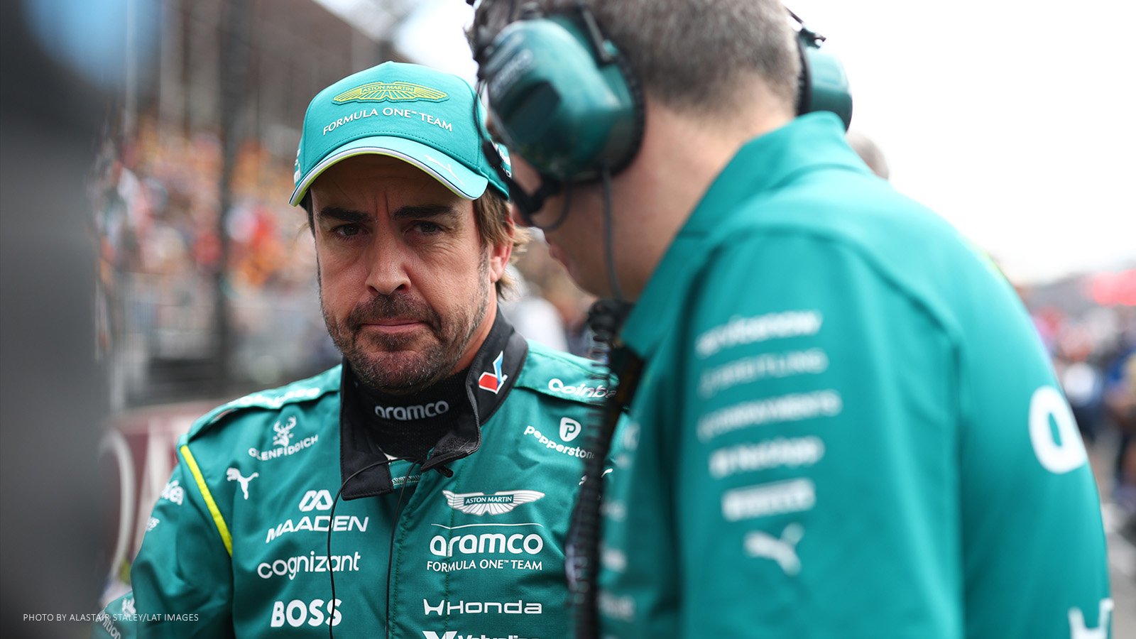 Fernando Alonso speaking with an Aston Martin team member wearing a headset.