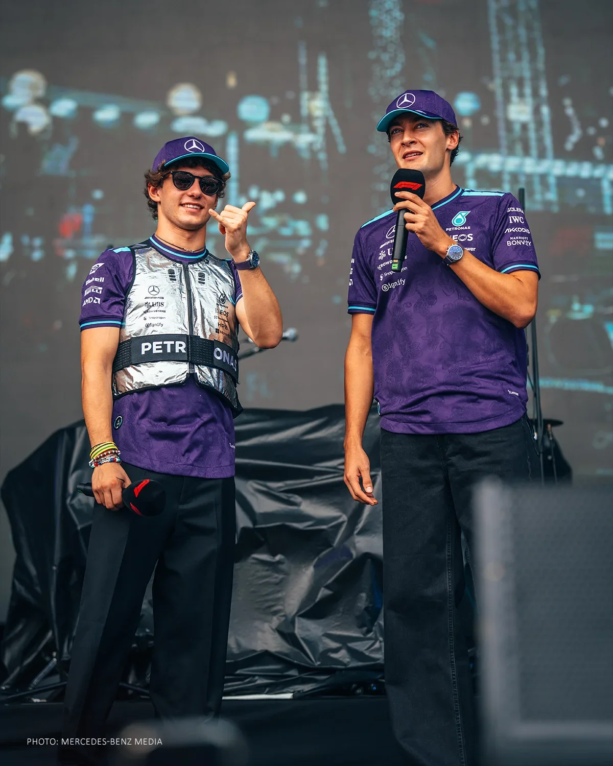 Kimi Antonelli and George Russell wearing purple Adidas Mercedes team shirts and caps during a Singapore Grand Prix fan appearance.