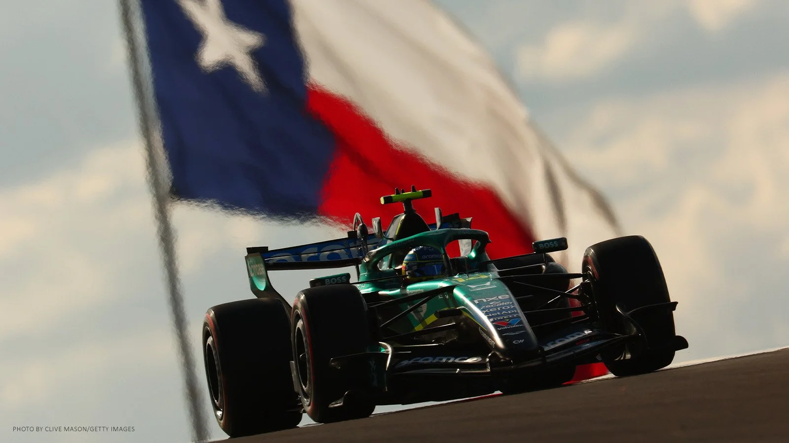Fernando Alonso driving his Aston Martin at Circuit of the Americas with the Texas flag in the background.