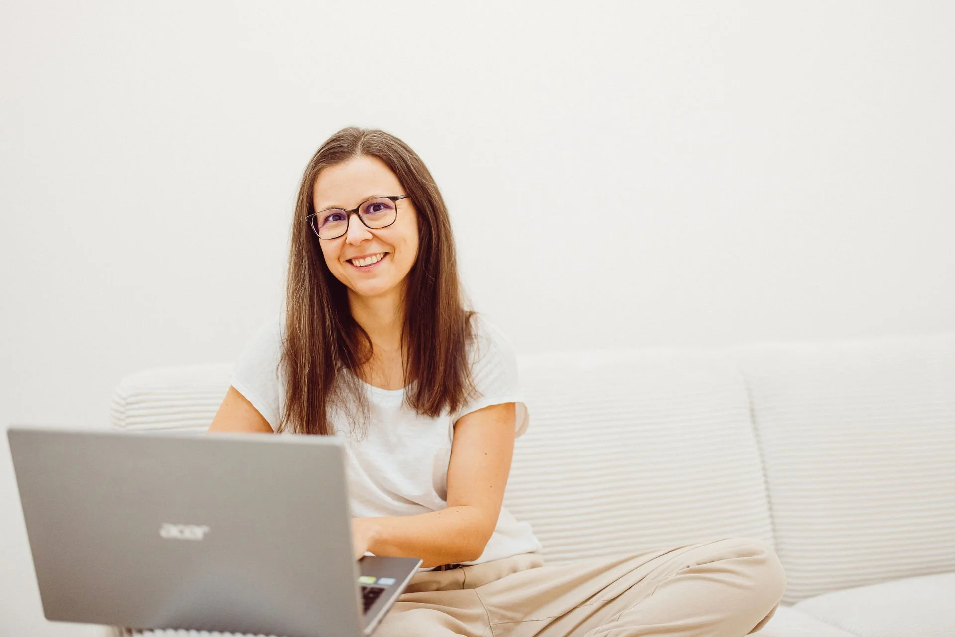 Tanja Heirens Coaching | Eine lächelnde Frau sitzt auf einem weißen Sofa und benutzt einen Laptop.