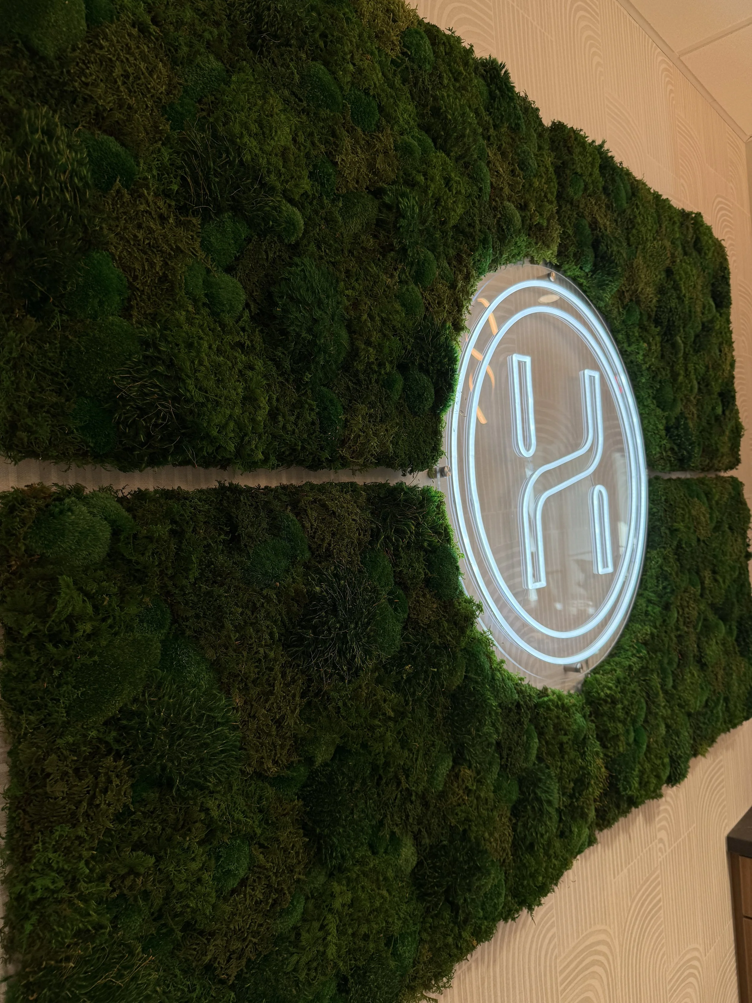 A green moss wall with a neon blue logo in the center.