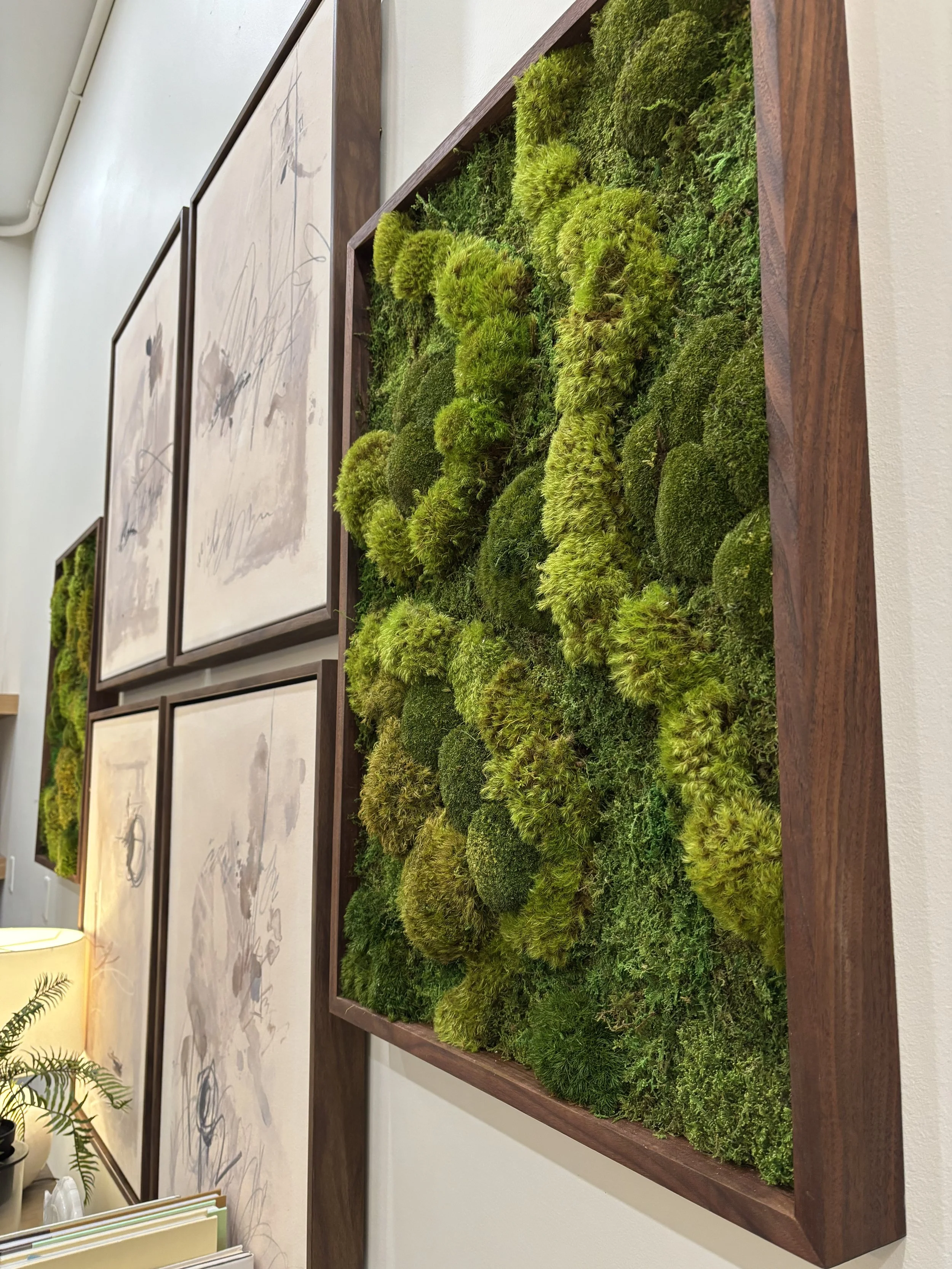 A wall-mounted wooden frame containing preserved green moss arranged as a decorative art piece.