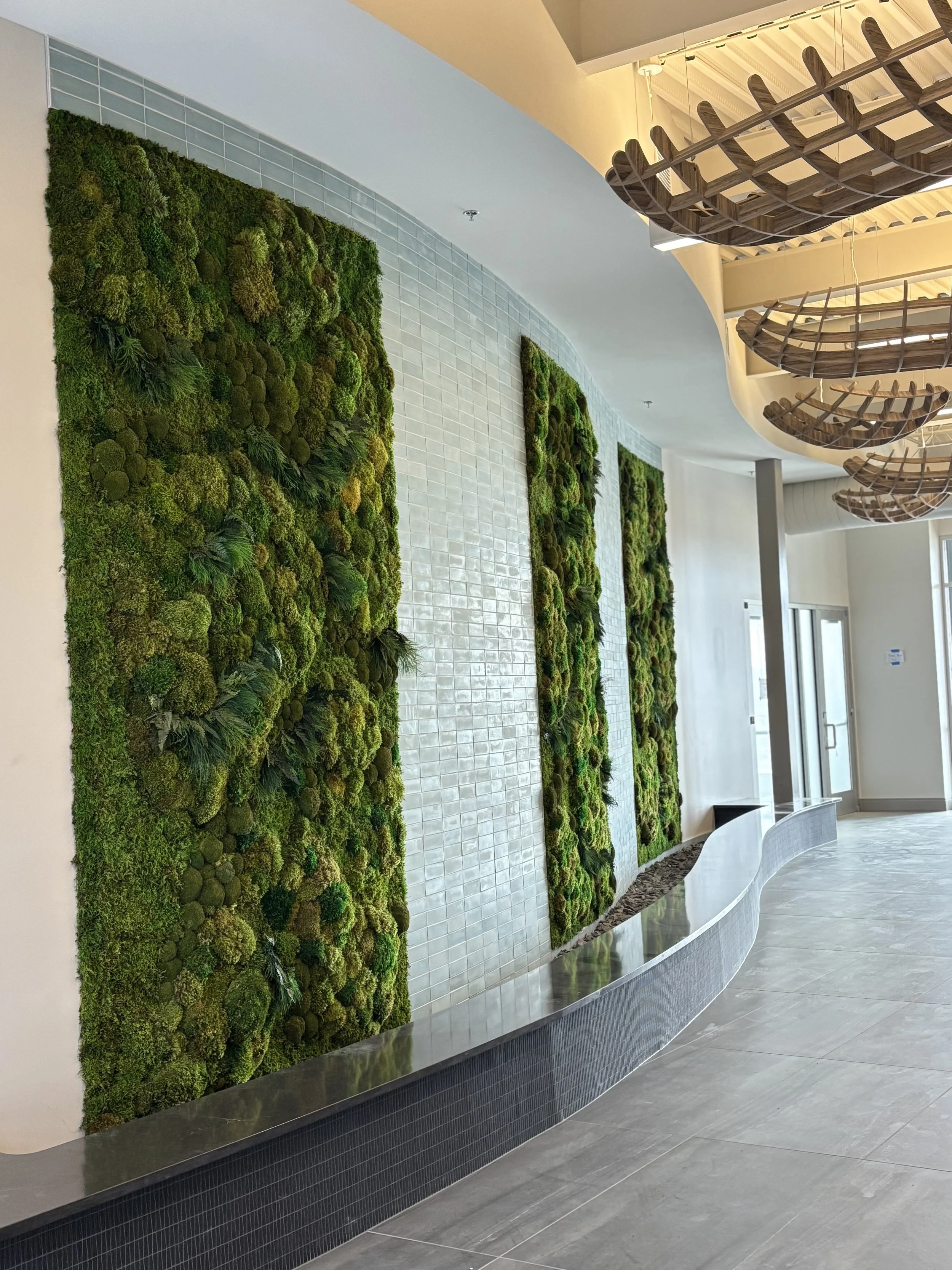 Indoor wall decorated with vertical green moss art and a curved metallic bench with a tiled wall in the background.