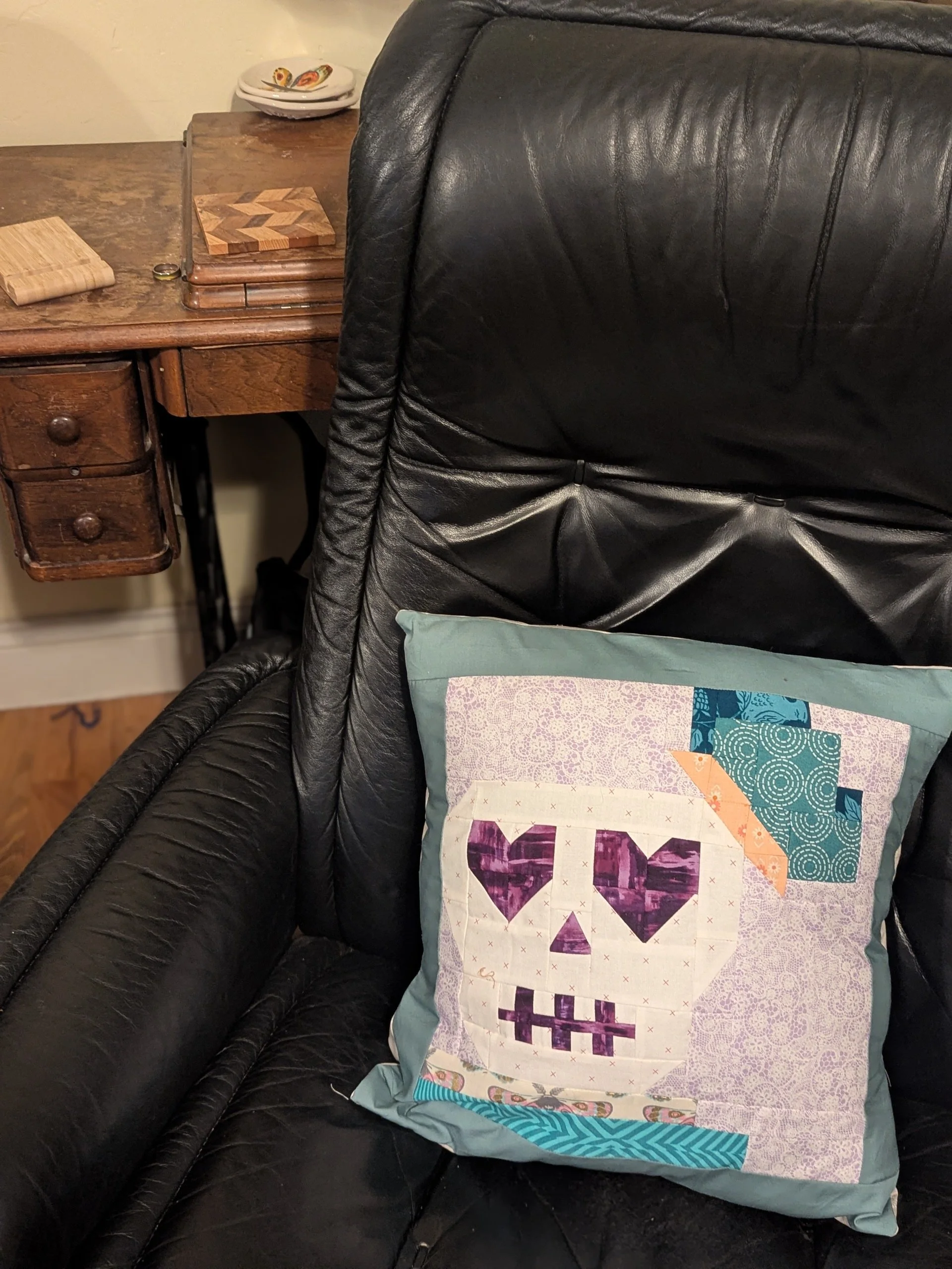 Uncle albert pillow in black chair with vintage sewing table in background.