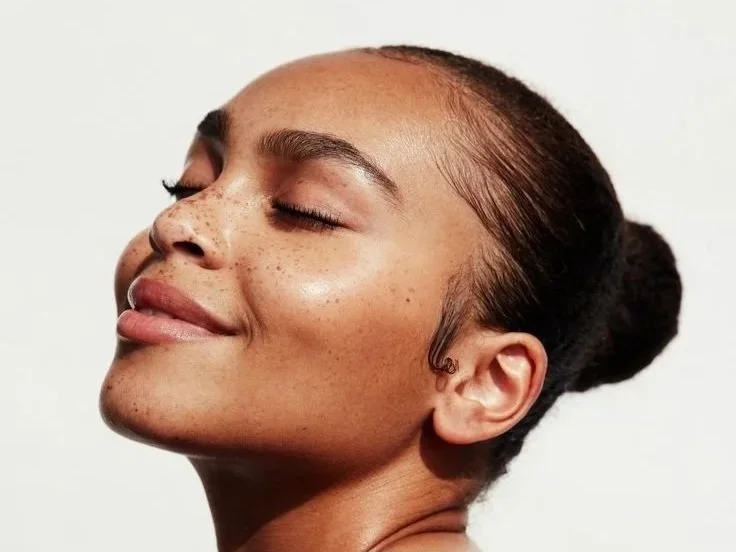 Close-up of a woman with smooth, glowing skin, closed eyes, and a serene expression, with her hair tied back.