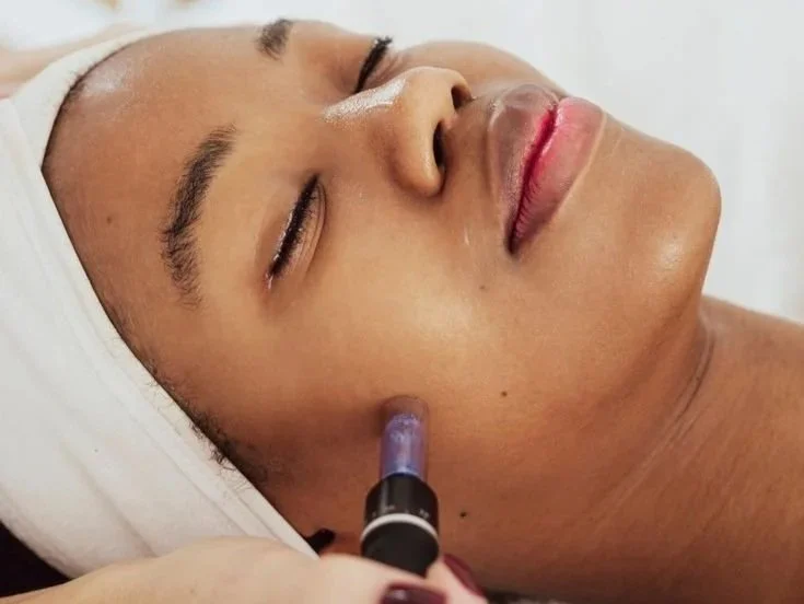 A woman with her eyes closed receiving a cosmetic treatment to her face with a nozzle applicator.