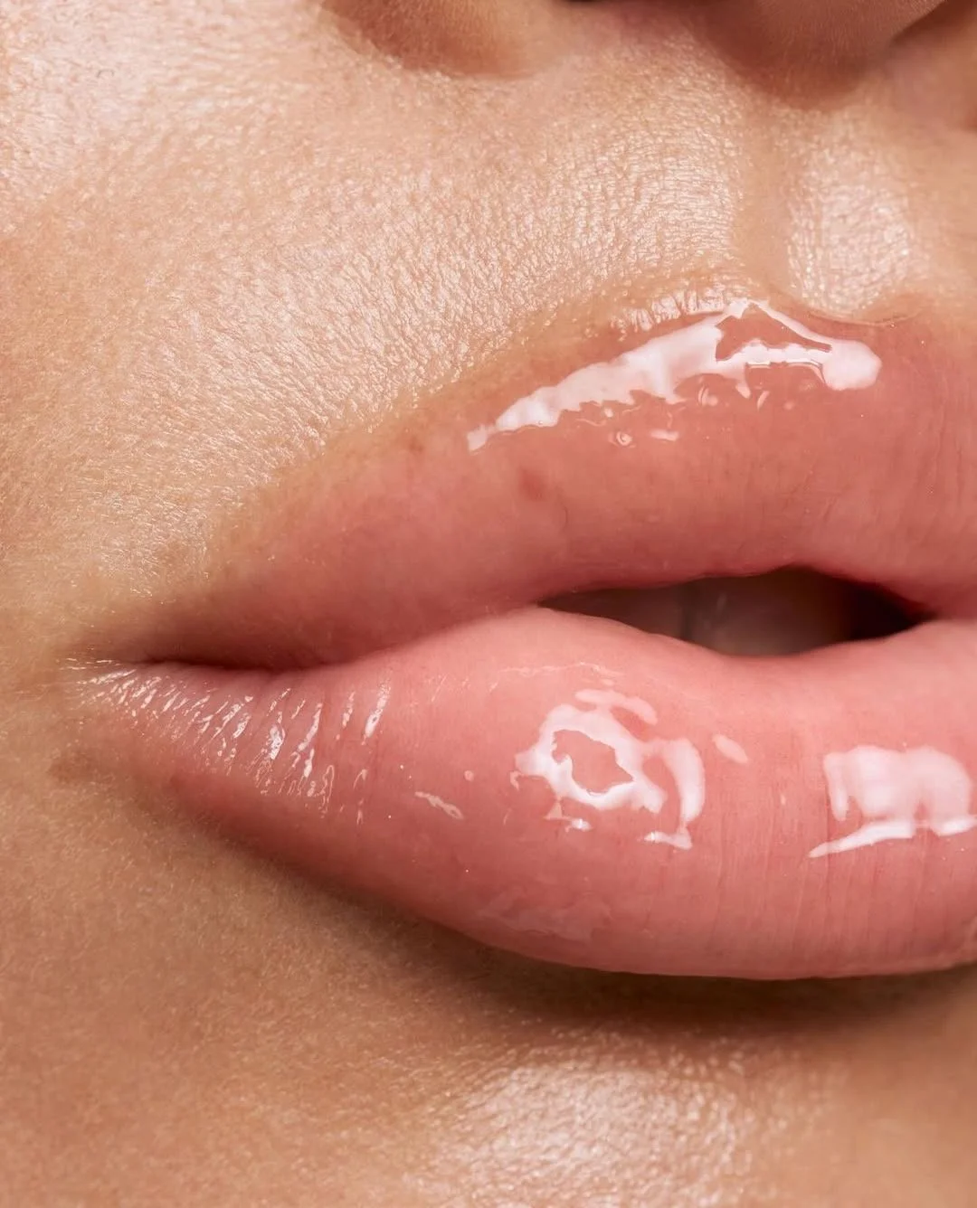 Close-up of lips with lip gloss, showing detailed skin texture and shiny appearance.