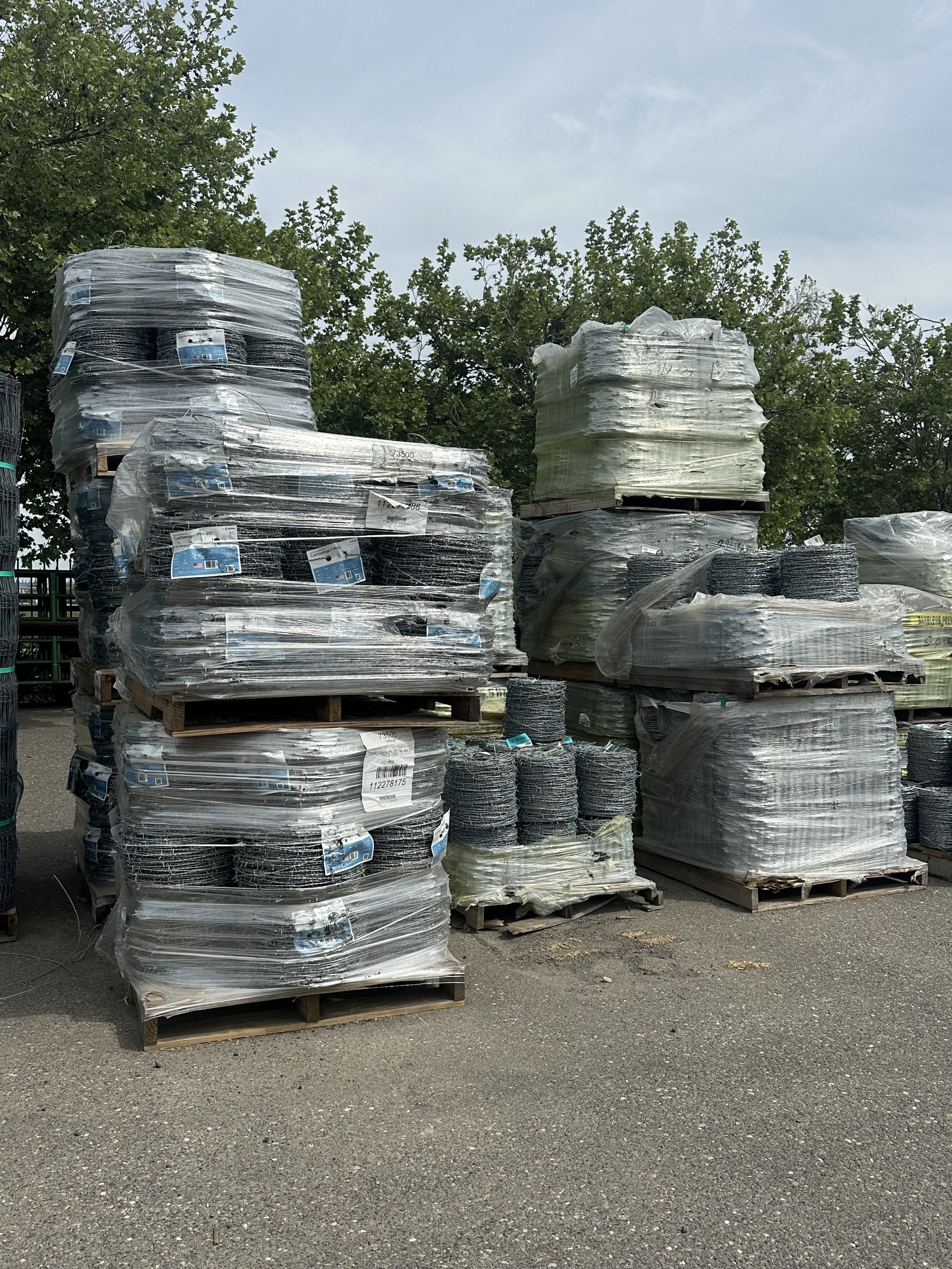 Stacks of wire fencing wrapped in plastic on wooden pallets outdoors.