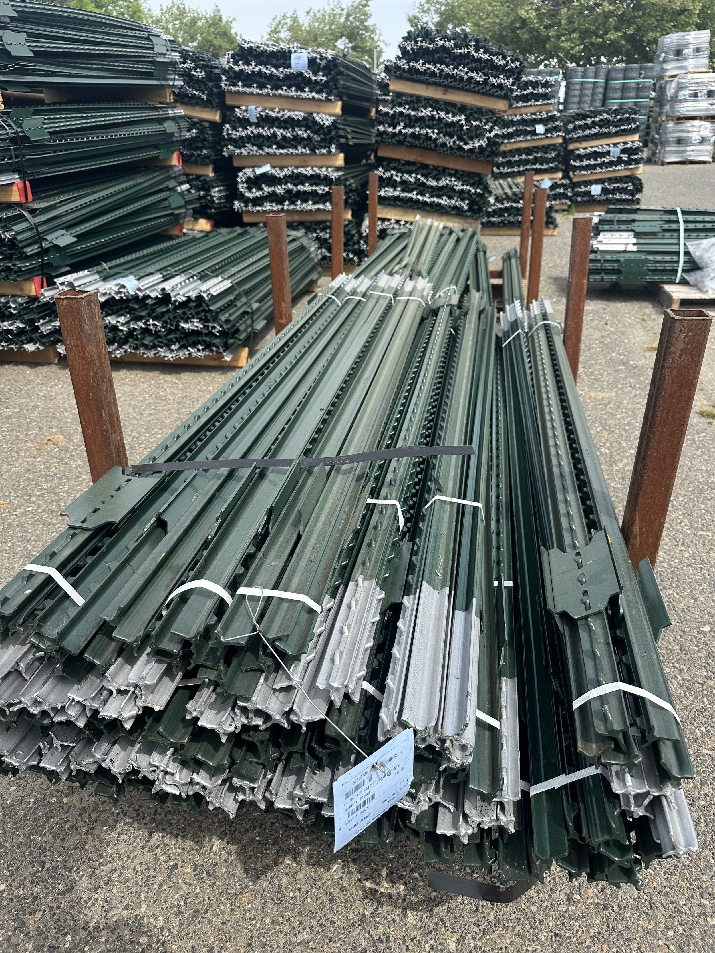 Stacks of green metal fence posts neatly arranged on pallets in an outdoor setting.