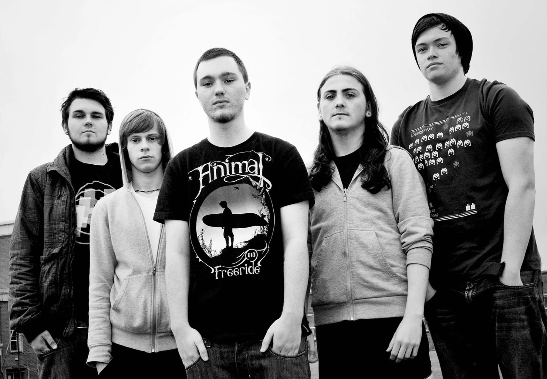 Black and white photo of five young men standing, one wearing a beanie and graphic T-shirts.