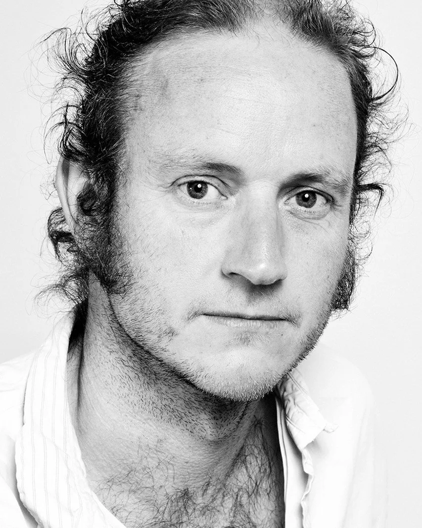Black and white portrait of a man with curly hair, wearing a light-colored shirt.