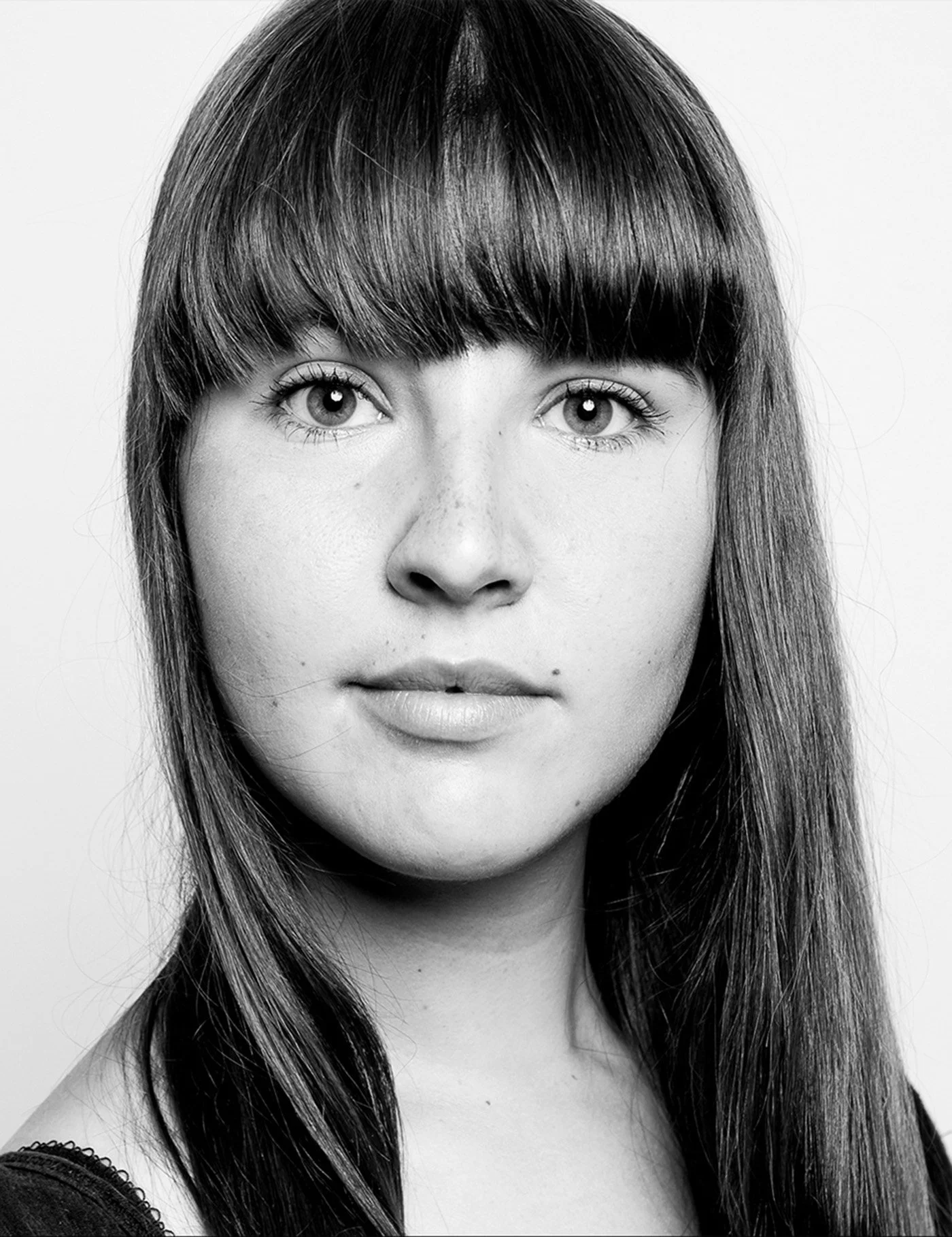Black and white close-up portrait of a young woman with long, straight hair and bangs, looking directly at the camera.