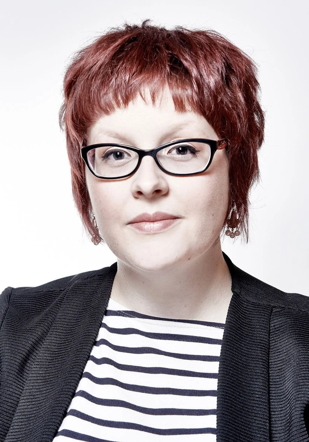Woman with short red hair and glasses, wearing a black blazer over a striped shirt, portrait photo.