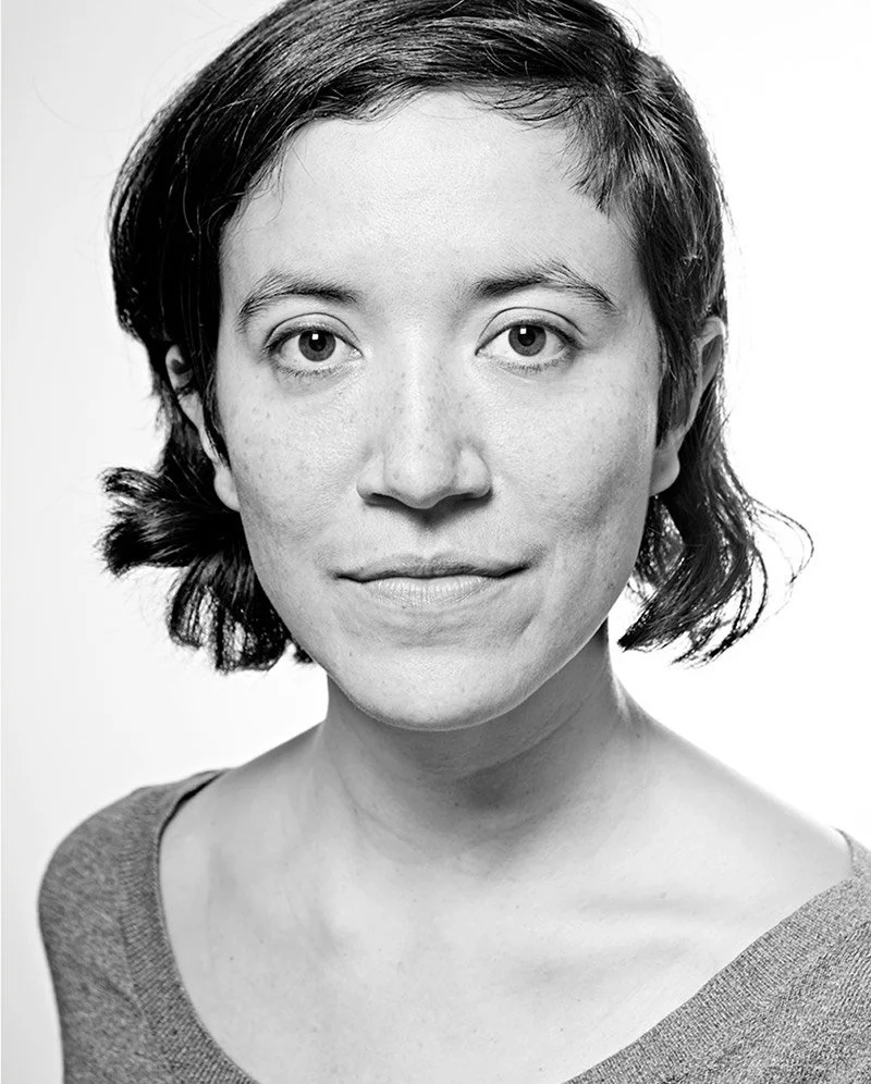 Black and white portrait of a person looking directly at the camera. They have short, wavy hair and are wearing a casual top.