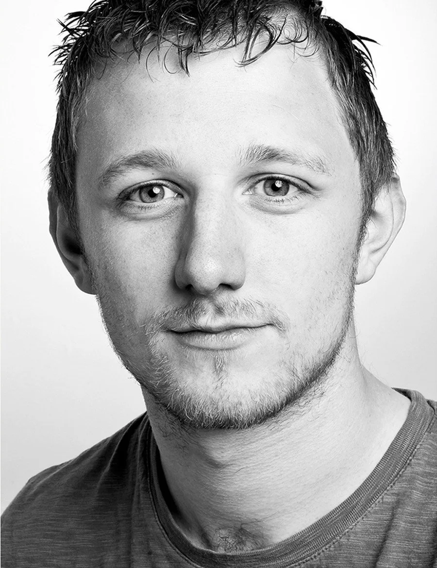 Black and white portrait of a man with short hair, wearing a t-shirt, facing the camera.