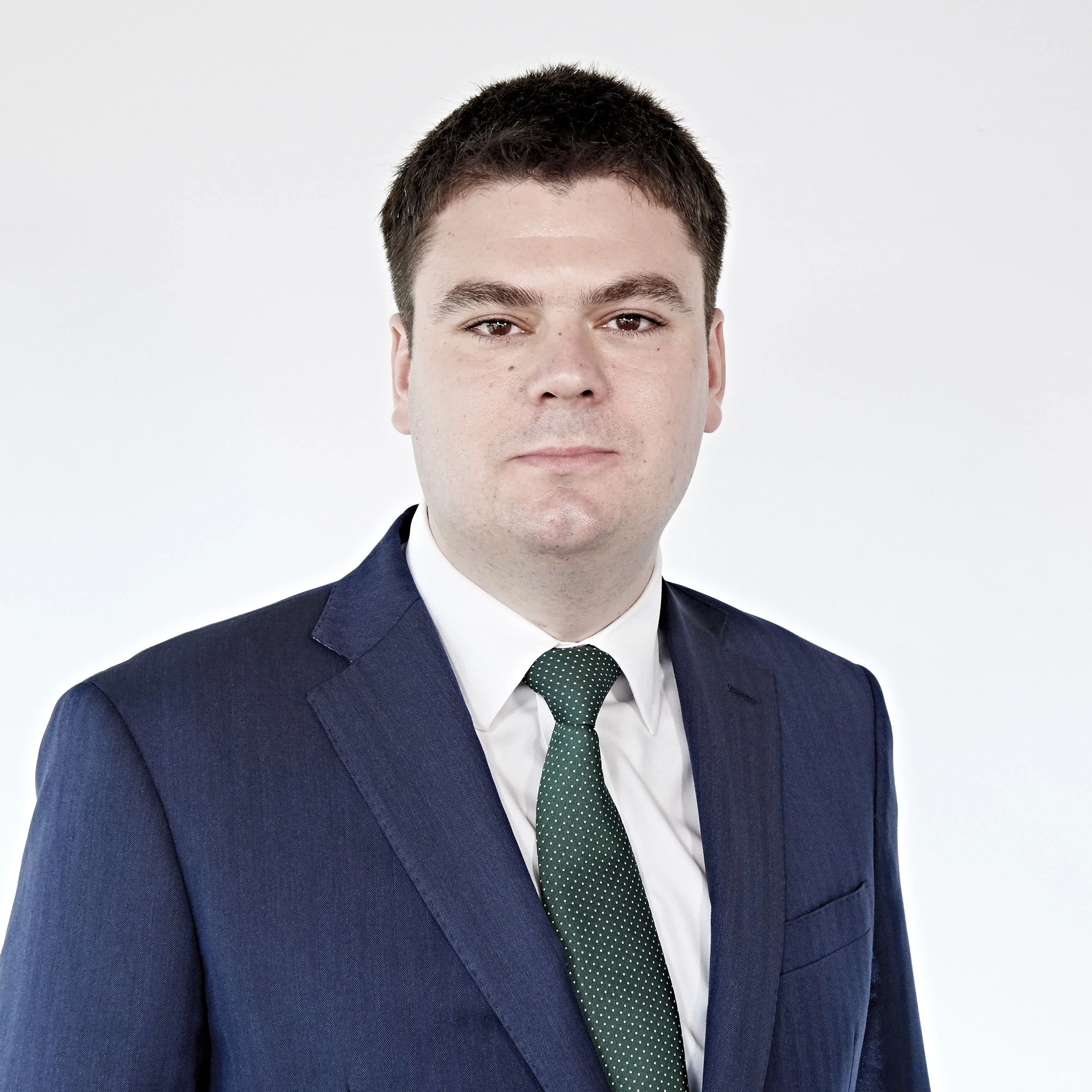 Man in a suit and tie against a plain background.