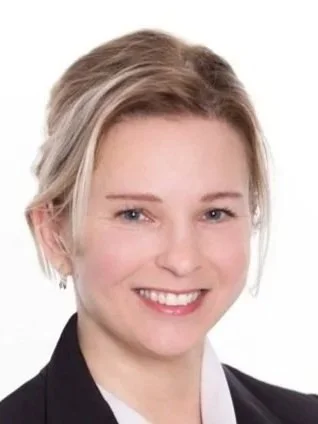 Professional woman with blonde hair, wearing a black blazer and white shirt, smiling against a white background.