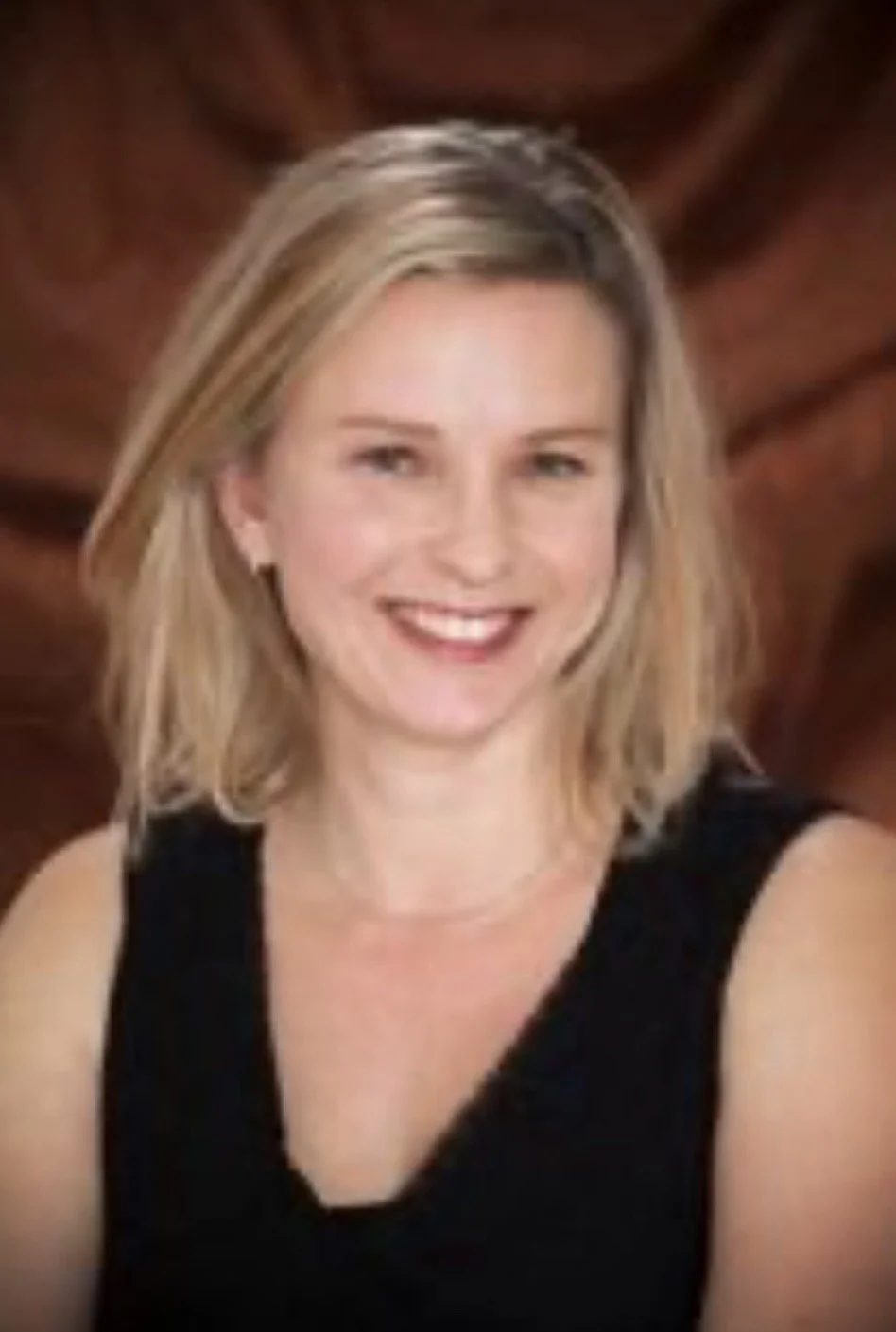 Professional woman with blonde hair, wearing a black blazer and white shirt, smiling against a white background.