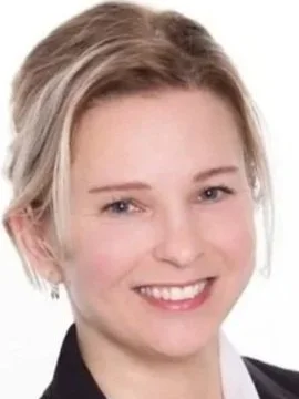 Professional woman with blonde hair, wearing a black blazer and white shirt, smiling against a white background.