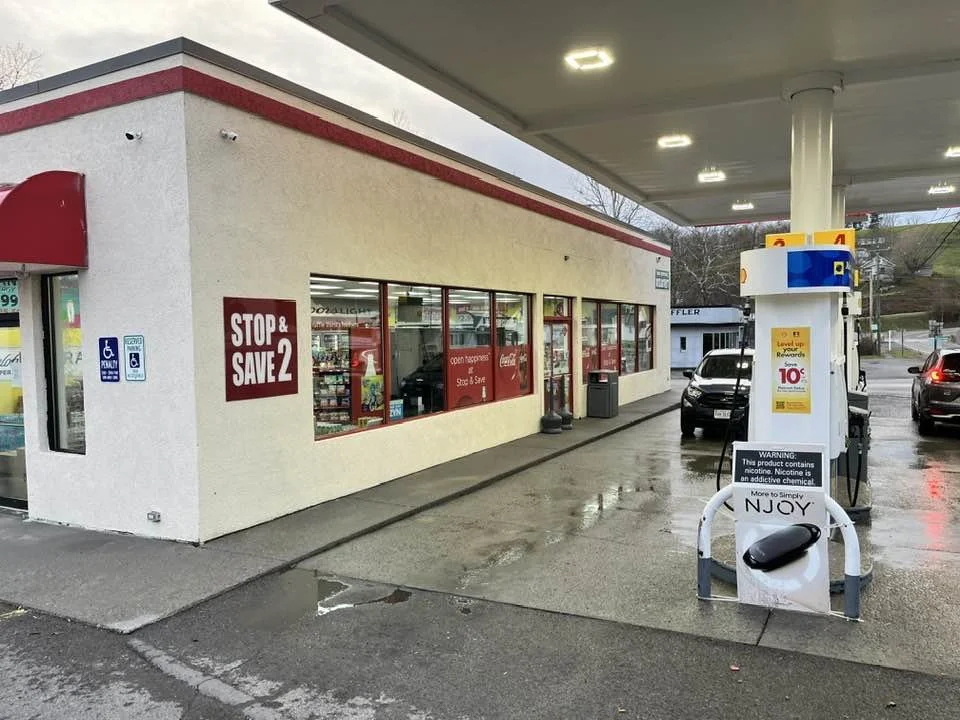 Gas station with a convenience store named "Stop & Save 2," featuring fuel pumps, parked cars, and advertising signage.