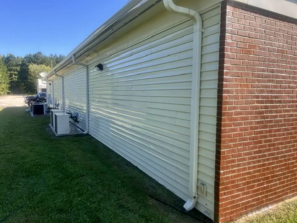 Exterior of a building with white siding and a brick corner, featuring air conditioning units and a downspout on a grassy area.