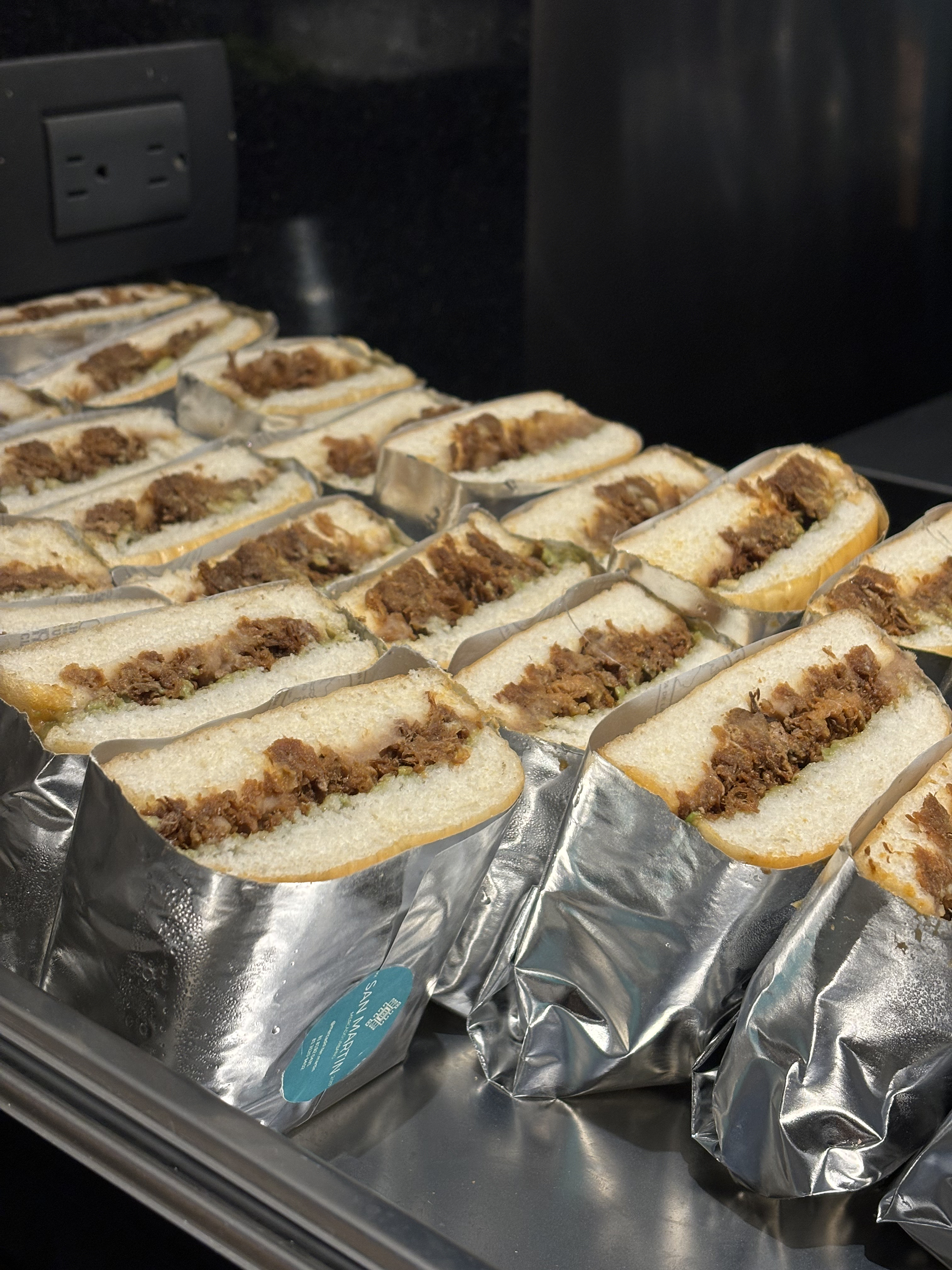 Multiple sandwiches with meat filling, wrapped in silver foil, placed on a tray.