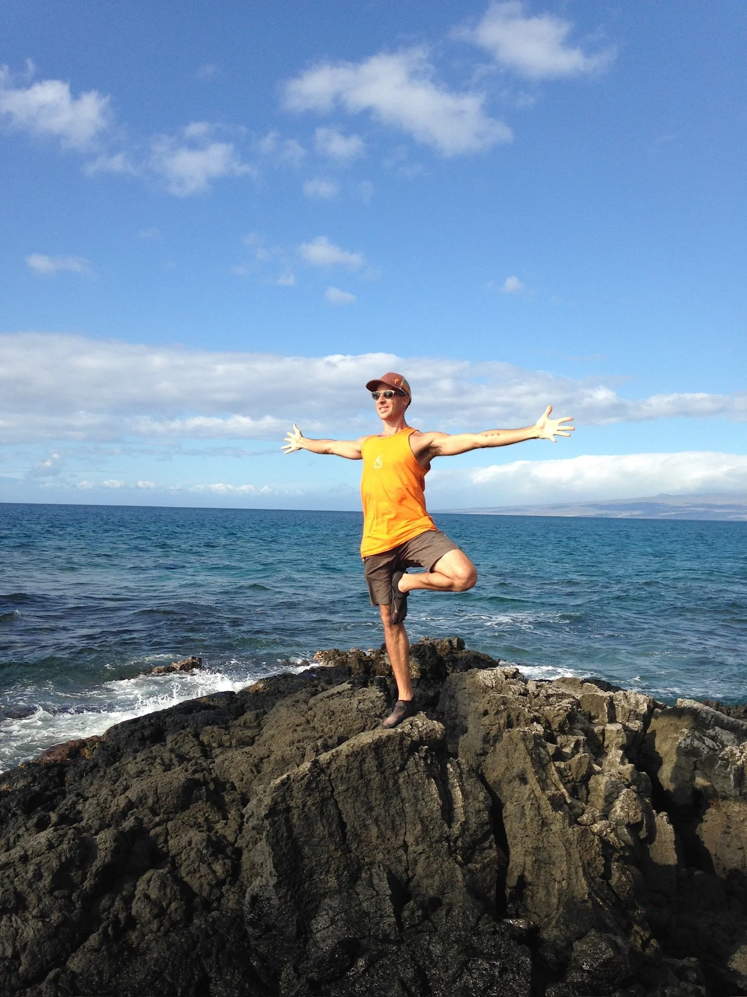 Yoga practitioner balancing on coastal lava rocks beside the ocean in Hawaii.