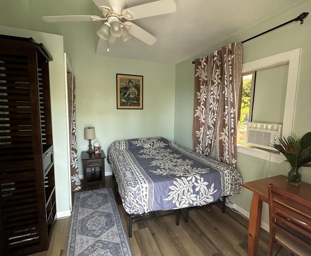 A single room with nicely made bed and tropical patterned comforter and curtains.