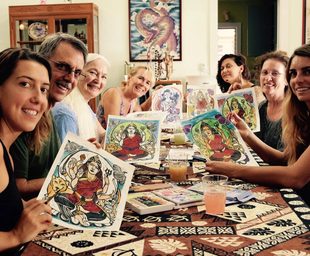 A smiling group of people hold up art pieces around a table.