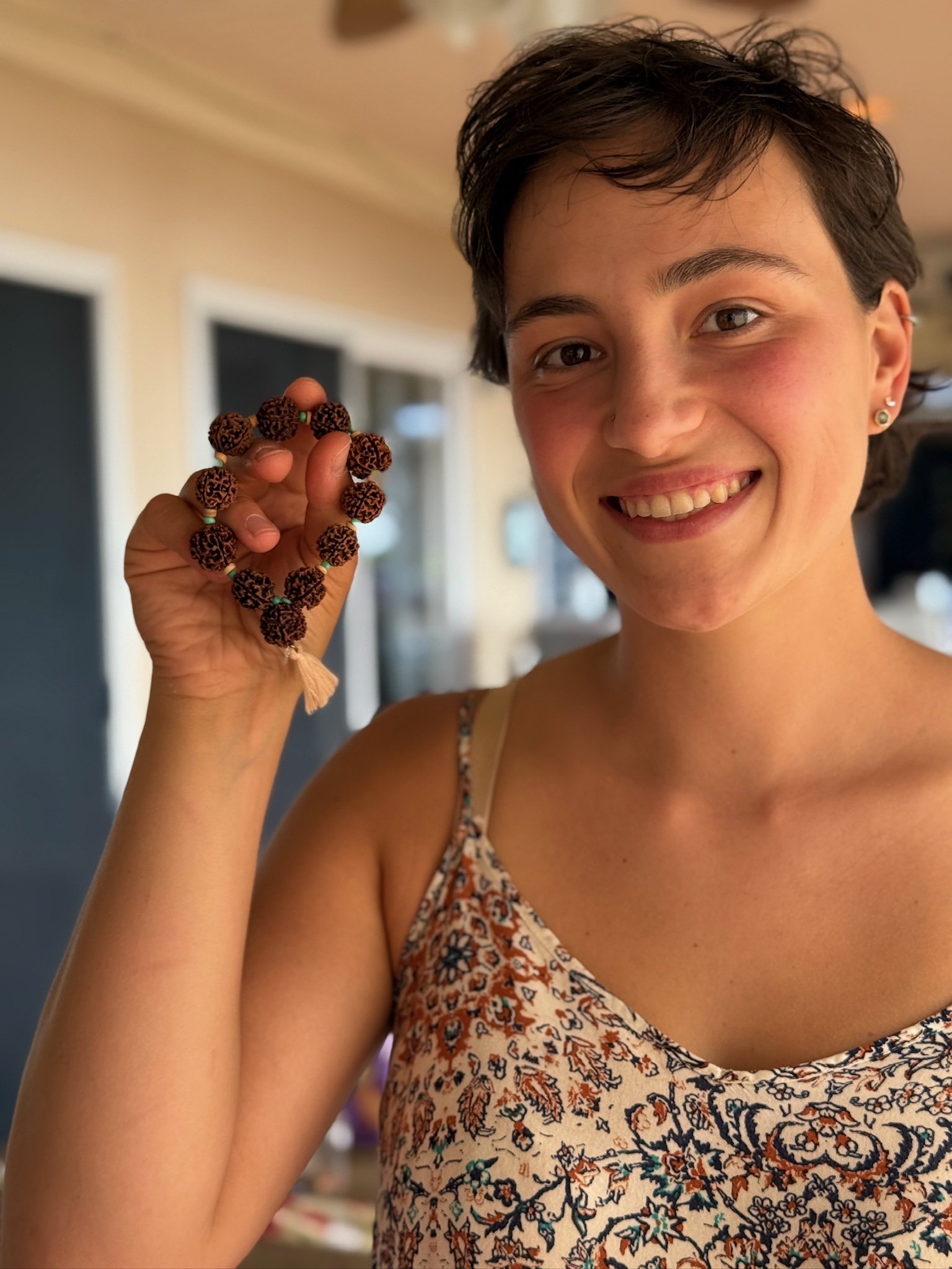 A young woman with short dark hair smiling and holding a beaded bracelet with dark beads in her hand.