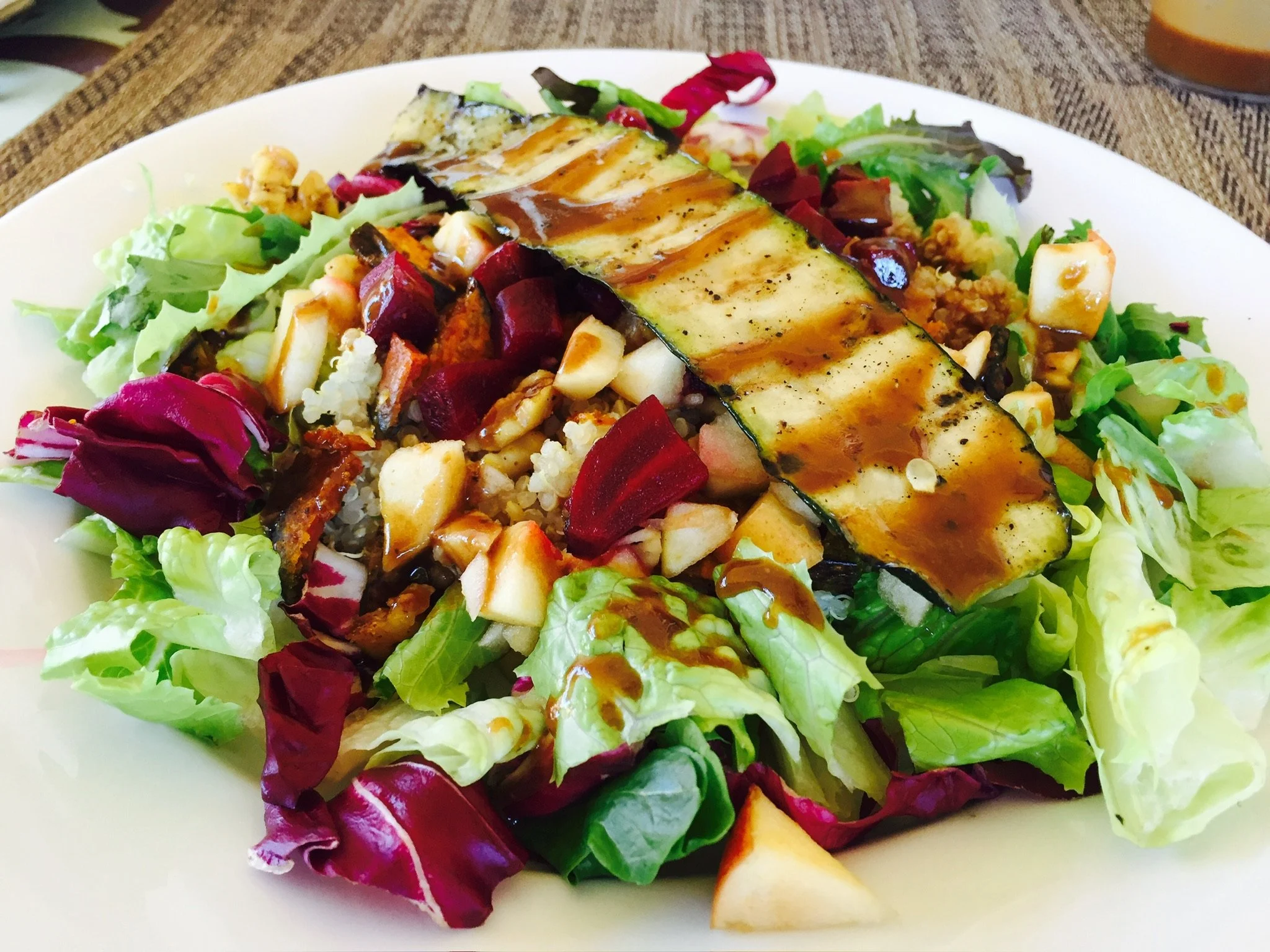 A plate of mixed salad with greens, chopped vegetables, cheese, and grilled zucchini, drizzled with dressing.
