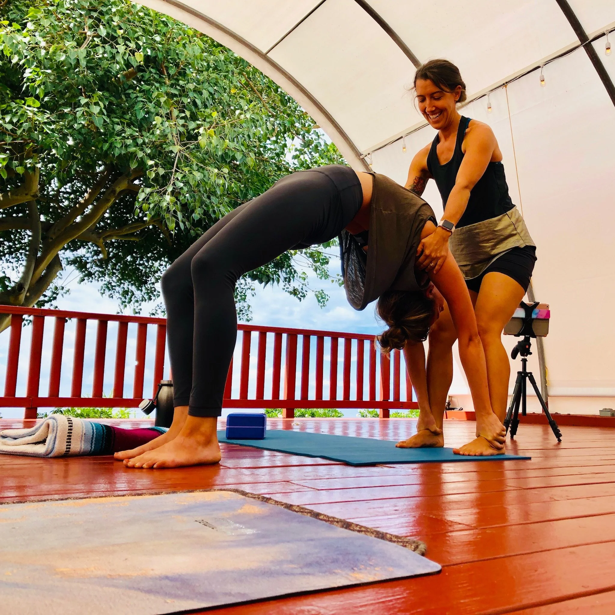 A yoga teacher assisting a student in a supported backbend.