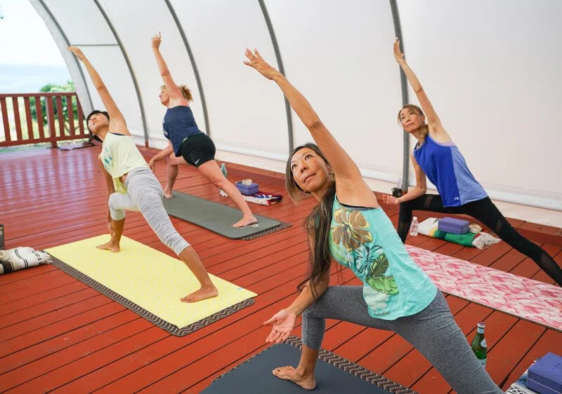 A group of female yogis hold a yoga pose with a wide stand extending one arm long over head.