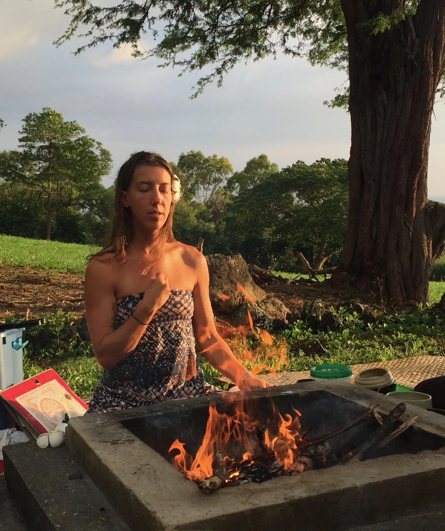 A woman seated beside a ceremonial fire outdoors at Konalani.