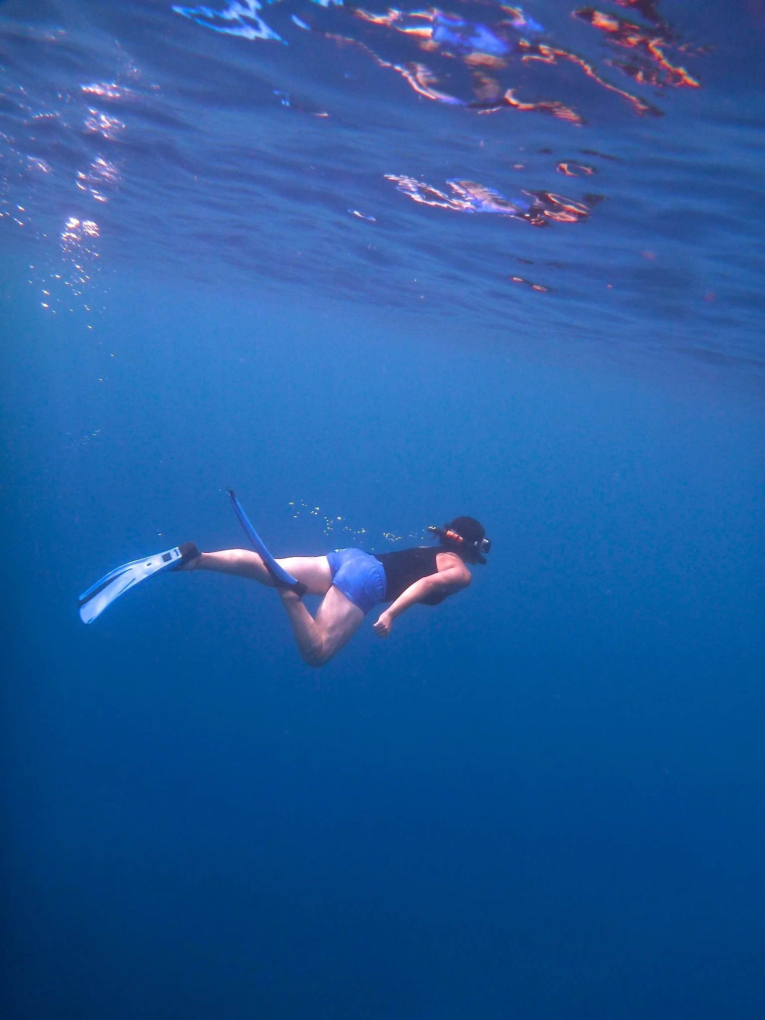 A person snorkeling underwater with a mask, fins, and a snorkel, swimming in clear blue water.