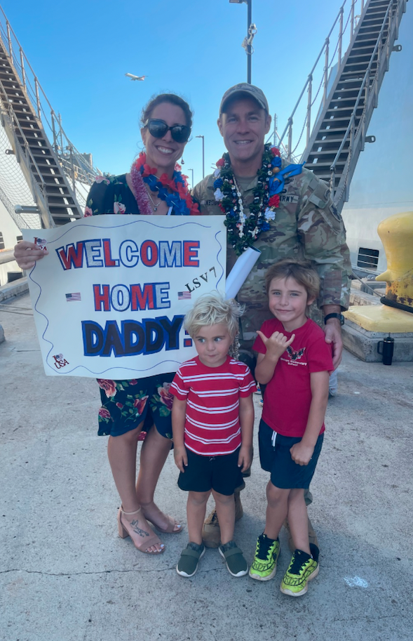 A military family reunited with a welcome-home sign and flower leis.