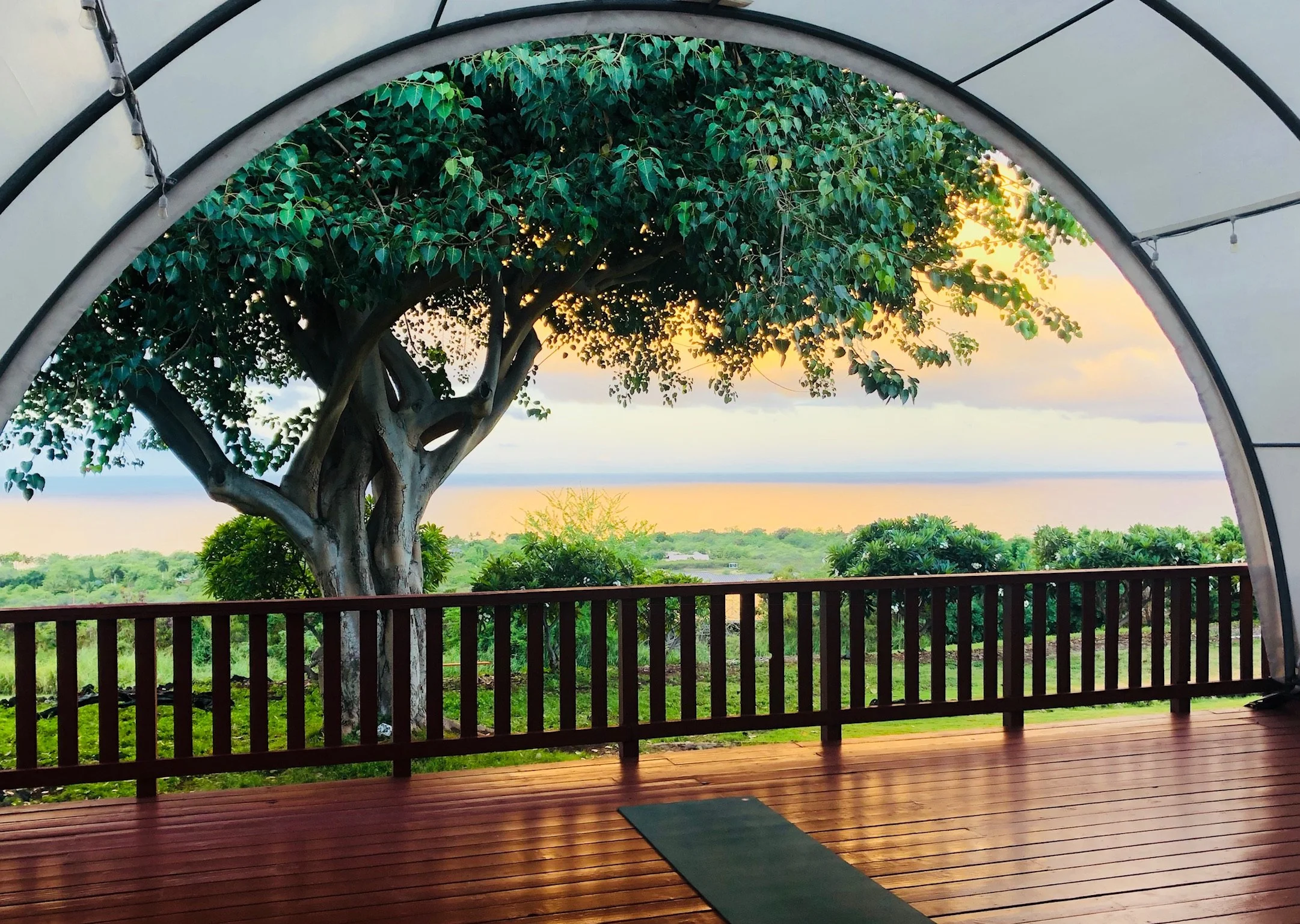 View from inside a covered outdoor deck overlooking a lush green landscape with trees, sky, and sunset in the distance.