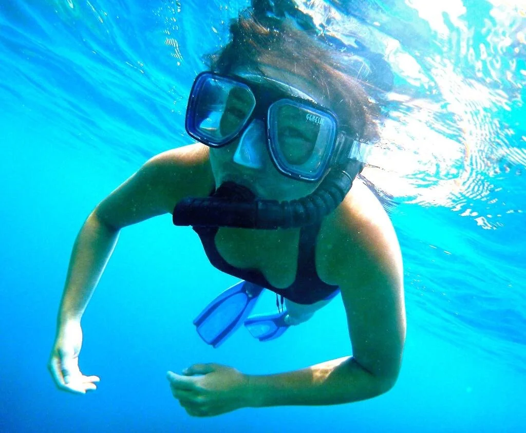A snorkling lady smiles with her eyes at the camera in crystal clear ocean.