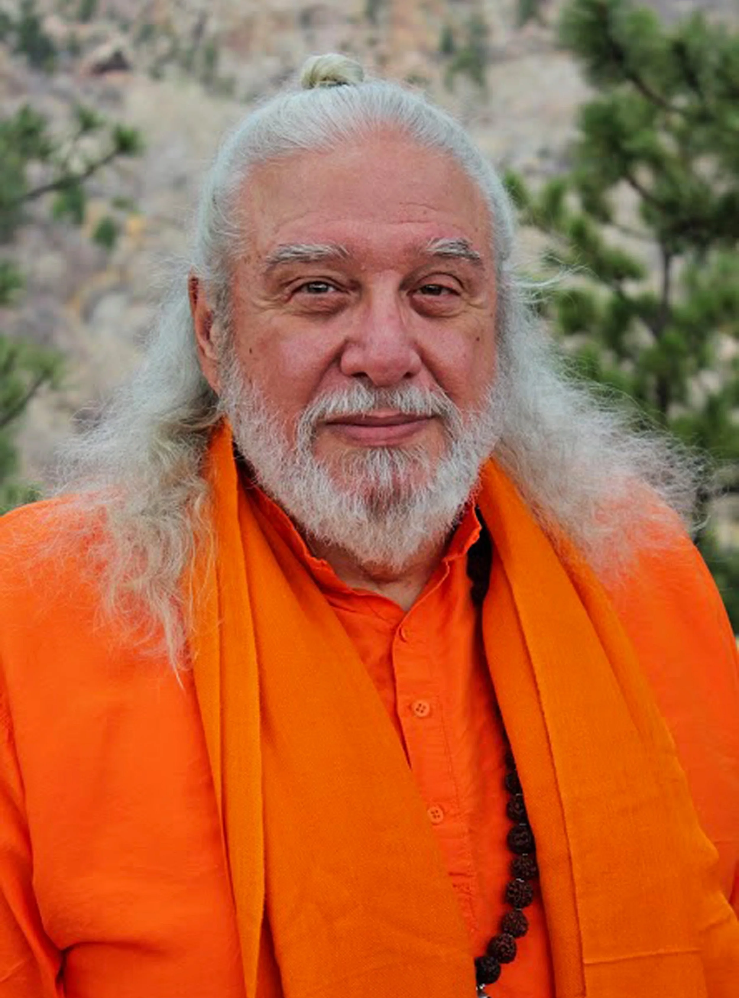 Sri Shambhavananda wearing orange robes and a mala necklace outdoors.