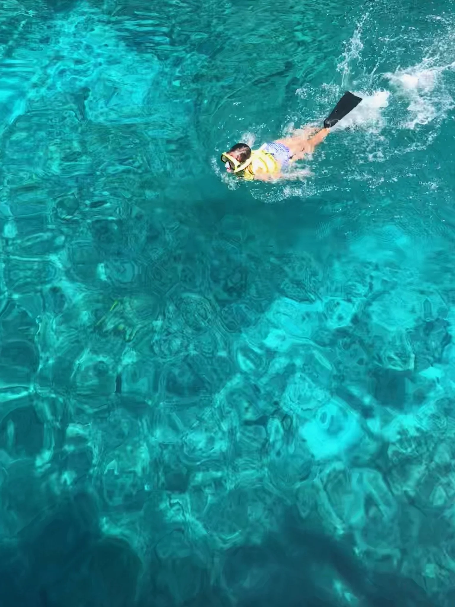 A snorkeler swimming in clear turquoise ocean water, viewed from above.