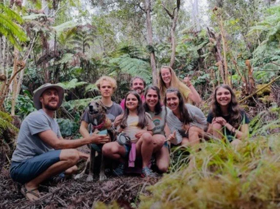 A group of yogis pose for a photograph in a tropical forest surrounded by leafy vegetation.