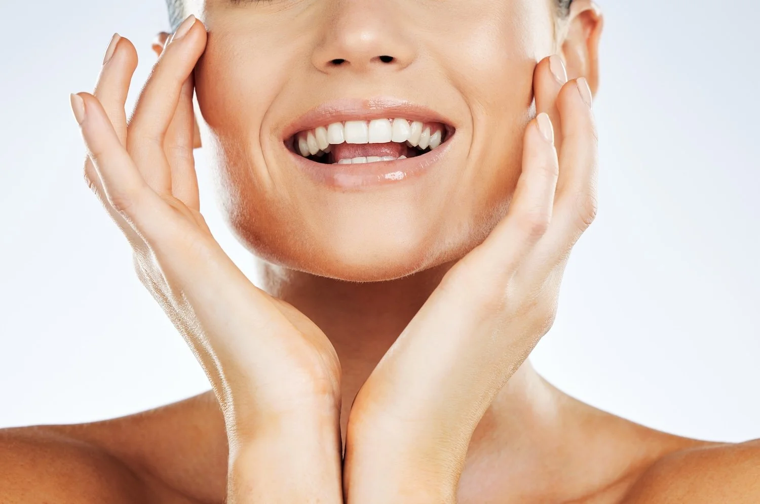 Close-up of a smiling woman's face with hands touching cheeks.
